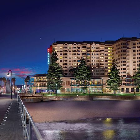 מלון גלנלג Stamford Grand Adelaide מראה חיצוני תמונה The photo shows a waterfront scene at dusk, featuring a large building lit up against a darkening sky. The architecture appears modern and prominent, with several windows illuminated. In the foreground, there is a walkway or pier with fencing along t