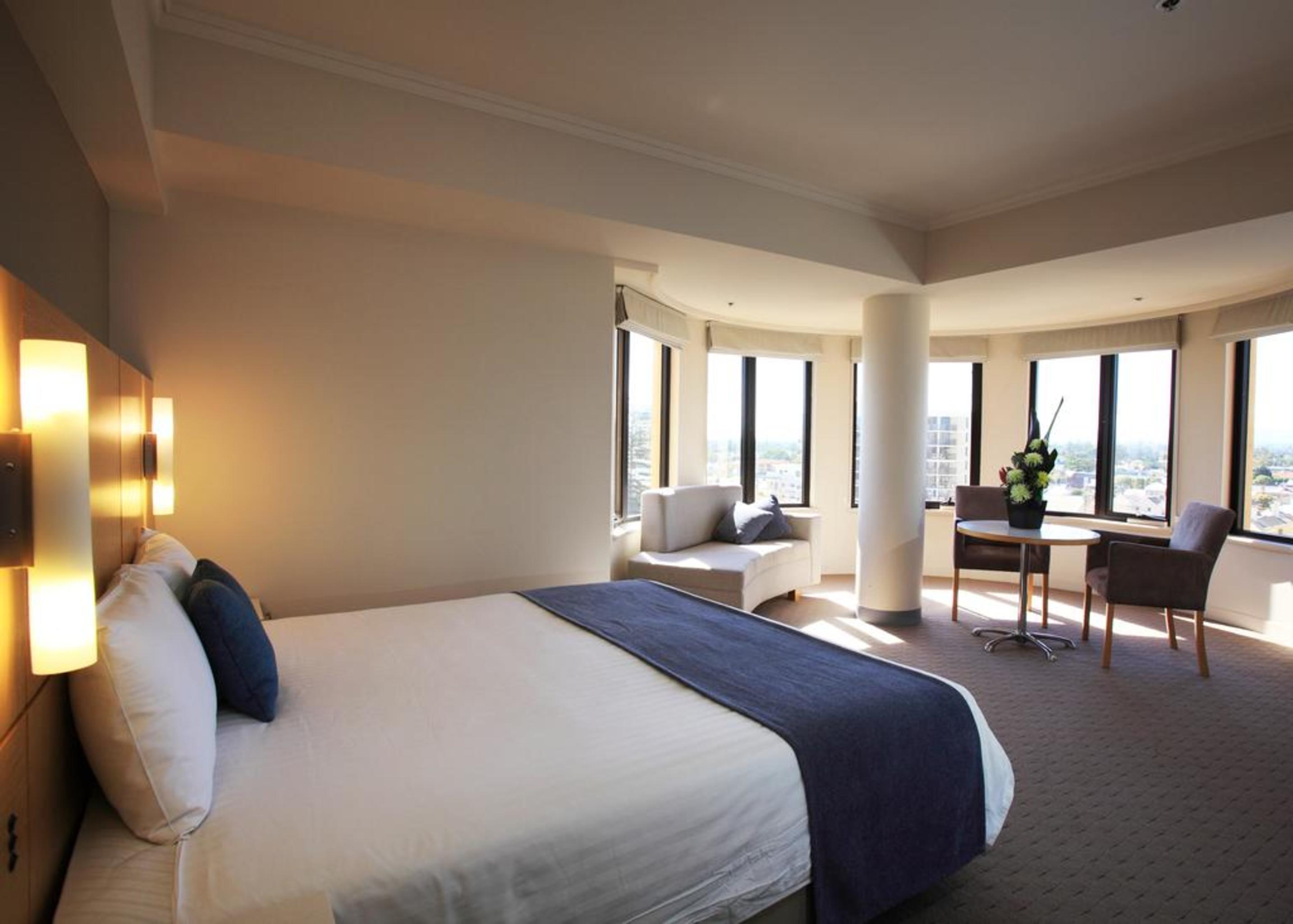מלון גלנלג Stamford Grand Adelaide מראה חיצוני תמונה The photo shows a hotel room with a modern and spacious design. There is a large bed with white linens and a dark blue throw blanket. The room features multiple windows that allow plenty of natural light, and there is a small seating area near the wi