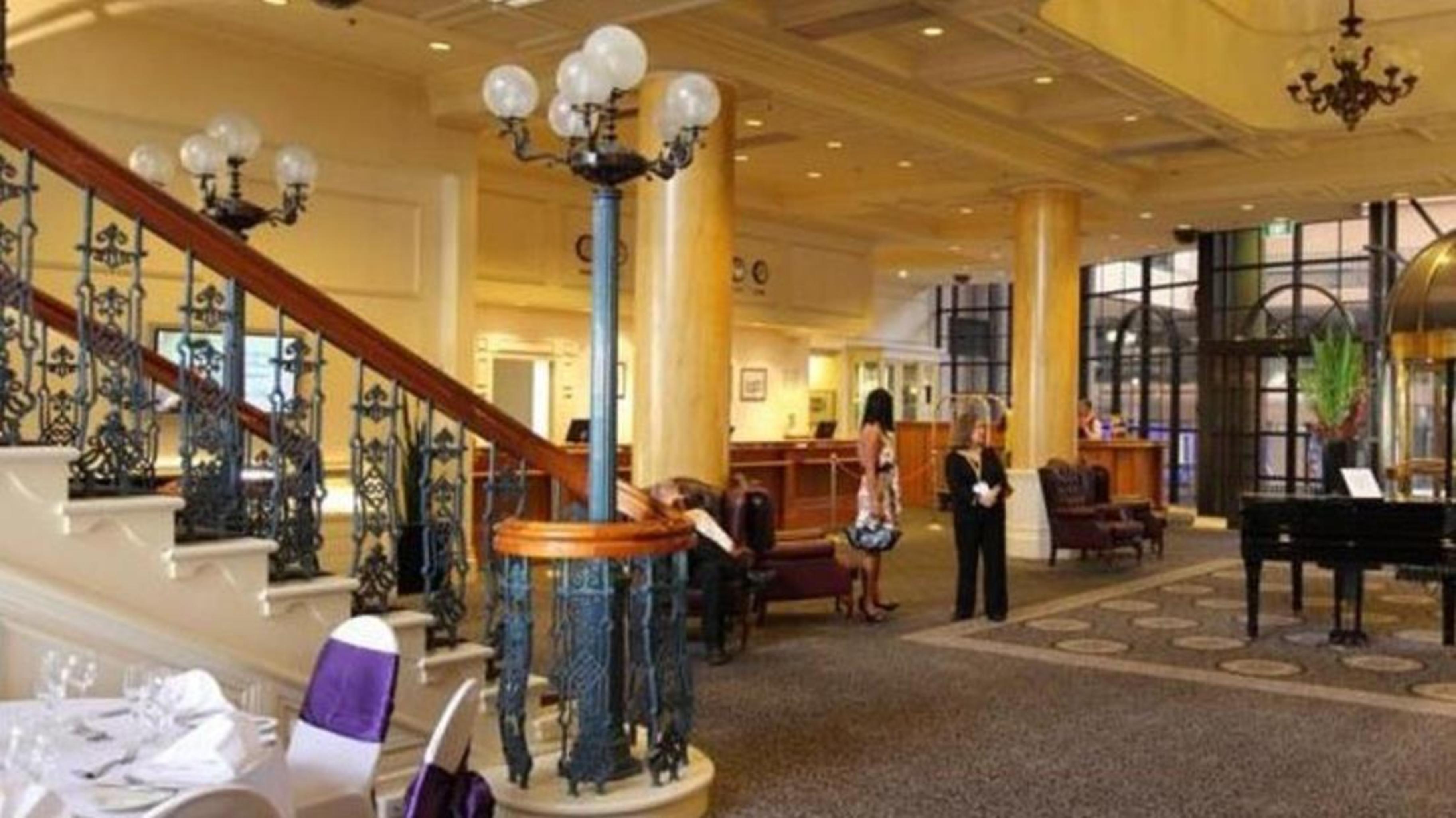 מלון גלנלג Stamford Grand Adelaide מראה חיצוני תמונה The photo shows the interior of a hotel lobby. It features a spacious area with a high ceiling and elegant decor. There is a staircase with a decorative railing leading to an upper level. In the foreground, some guests and staff are present, and ther