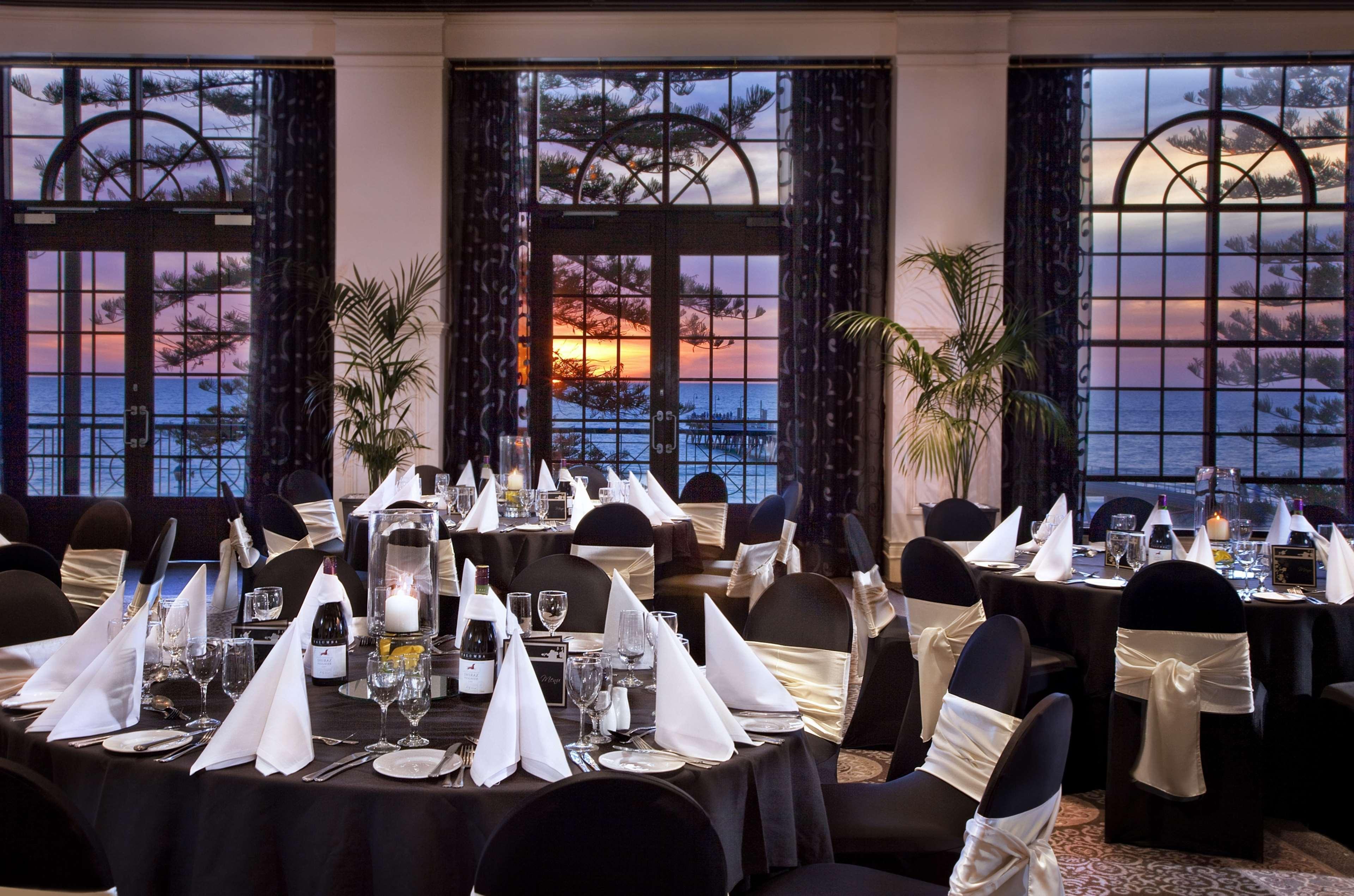 מלון גלנלג Stamford Grand Adelaide מסעדה תמונה The photo shows an elegantly decorated dining room with a beautiful view. The tables are set with black tablecloths and white napkins folded in a triangular shape. There are glassware and silverware neatly arranged at each setting. The room is adorne