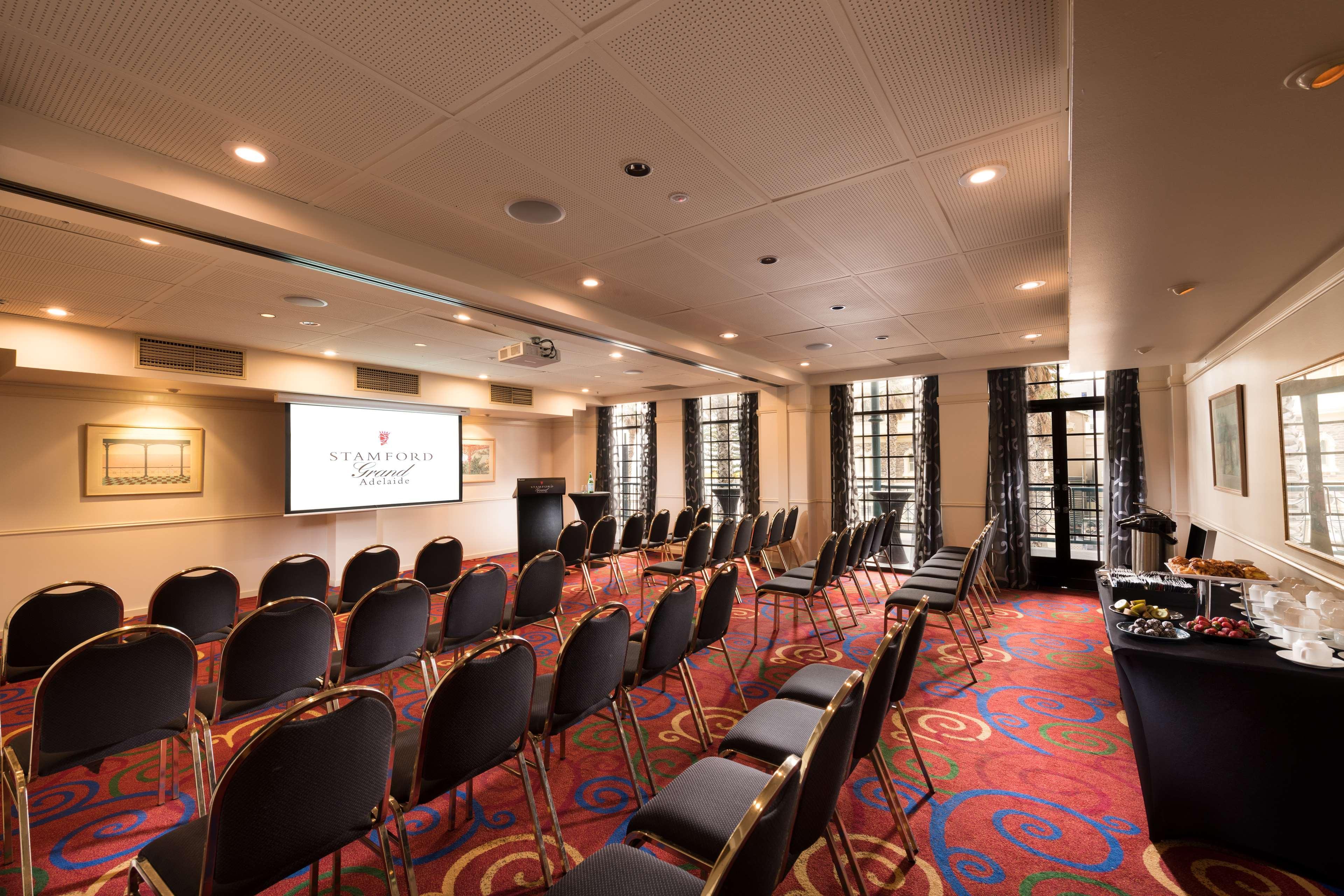 מלון גלנלג Stamford Grand Adelaide מראה חיצוני תמונה The photo shows a conference room set up for an event. There are rows of black chairs arranged in a semicircular formation facing a presentation screen at the front. The room features large windows that allow natural light to enter, and the flooring 