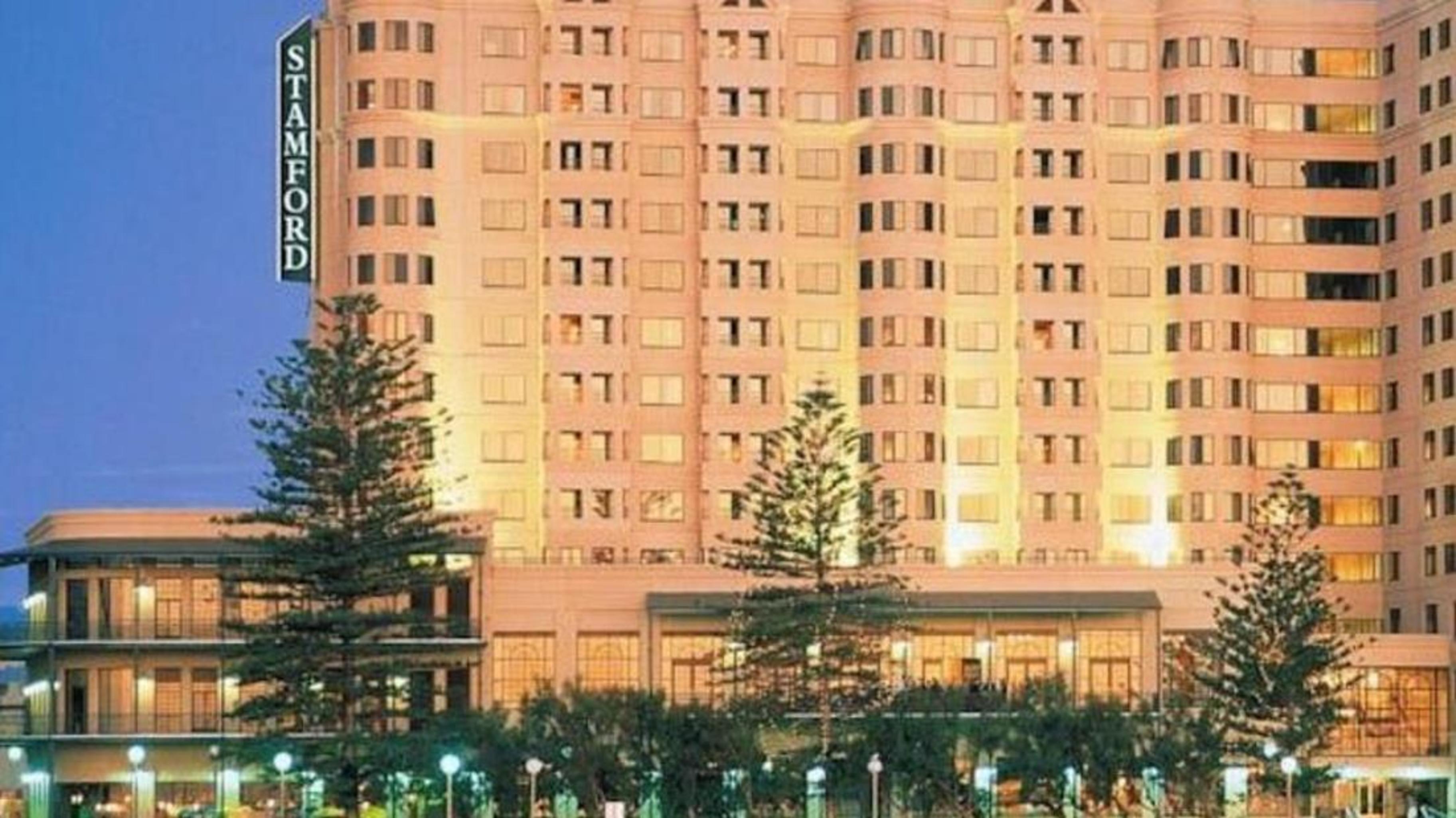 מלון גלנלג Stamford Grand Adelaide מראה חיצוני תמונה The photo shows a tall, modern building illuminated at night, likely a hotel, with the name "Stamford" prominently displayed on its side. Surrounding the building are several palm trees and landscaped areas, suggesting a tropical or coastal location.
