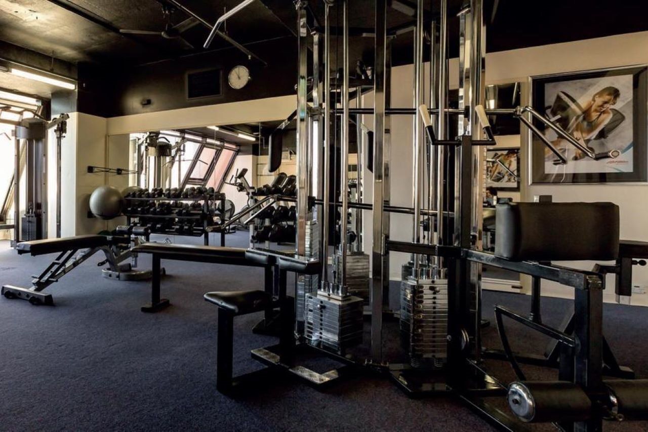 מלון גלנלג Stamford Grand Adelaide מראה חיצוני תמונה The photo shows a gym interior with various exercise equipment. In the foreground, there is a multi-station cable machine, which has several adjustable weights and pulleys for a variety of strength training exercises. To the side, there's a bench and