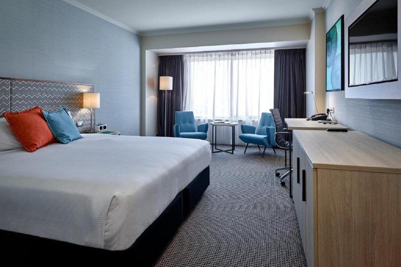 מלון גלנלג Stamford Grand Adelaide מראה חיצוני תמונה The photo shows a modern hotel room with a clean and minimalist design. In the center, there is a large, neatly made bed with white linens and two decorative pillows, one orange and one blue. To the right, there is a small wooden cabinet with a telev